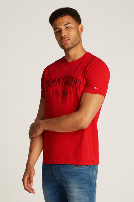 T-shirt rouge à manches courtes de TOMMY JEANS, avec une impression de logo et porté avec un jean bleu.