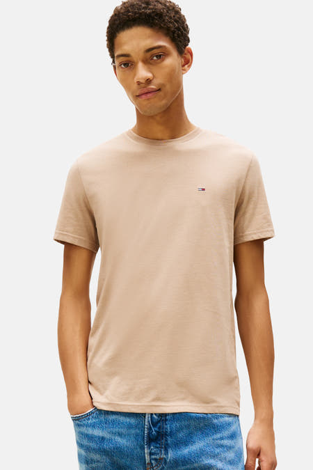 Beige T-shirt met korte mouwen van Tommy Jeans, met klein logo op de borst, gedragen met een blauwe jeans.

