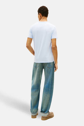 T-shirt bleu à manches courtes de TOMMY JEANS, vu de derrière, associé à des jeans larges et des chaussures en suède.