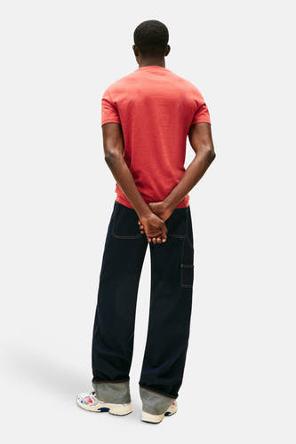 Rood T-shirt met korte mouwen van Tommy Jeans, achterkant, met donkere jeans en witte sneakers.
