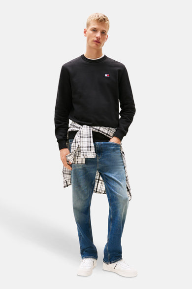 Pull noir de TOMMY JEANS, avec un chemisier à carreaux autour de la taille et des jeans bleus.