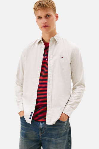 Kaki hemd met lange mouwen van TOMMY JEANS, gedragen over een gestreept T-shirt en jeans.