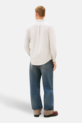 Man van achteren in gestreepte overhemd, wijde jeans en leren schoenen.