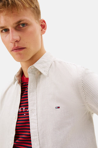 Man met blond haar draagt gestreept overhemd over rood-blauwe gestreepte T-shirt.