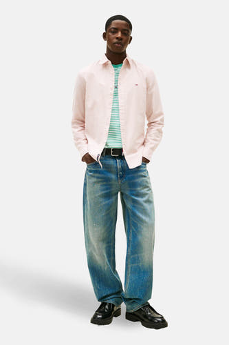 Rood, gestreept overhemd met lange mouwen van TOMMY JEANS, gedragen over een gestreept shirt en gecombineerd met wijde jeans en zwarte schoenen.