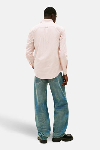 Man met rug naar camera, roze gestreept overhemd, wijde jeans en zwarte schoenen.