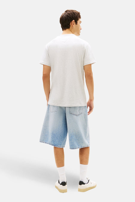 Grijs T-shirt met korte mouwen van TOMMY JEANS, achterzijde gezien, gecombineerd met wijde denim shorts, witte sokken en crèmekleurige sneakers.
