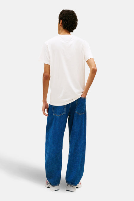 Wit T-shirt met korte mouwen van Tommy Jeans, gezien van achteren, gedragen met wijde, blauwe jeans en witte sneakers.
