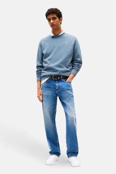 Blauwe sweater van TOMMY JEANS, gedragen over een wit shirt met jeans en witte sneakers.
