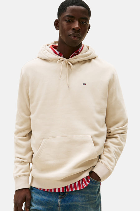 Pull-over beige avec capuche de TOMMY JEANS, porté avec un chemisier rayé rouge et blanc en dessous et des jeans bleus, vu de dos.