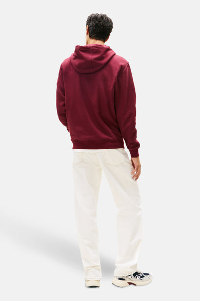 Gilet de Bordeaux avec capuche TOMMY JEANS, vu de dos, associé à des jeans blancs et des baskets colorées.