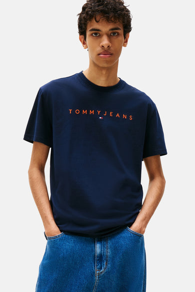 T-shirt bleu à manches courtes de TOMMY JEANS, porté avec un pantalon de travail.