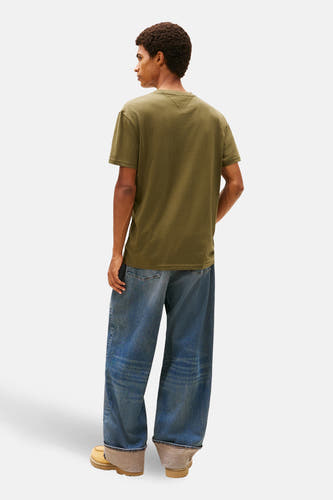 T-shirt vert avec manches courtes de TOMMY JEANS, doté d'un petit détail sur le dos, associé à des jeans larges et des chaussures en cuir suédé.