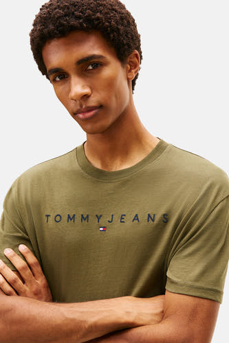 T-shirt vert de man mantes courtes TOM TOMMY JEANS, avec logo marque sur la poitrine, porté par un homme les les bras croisés.