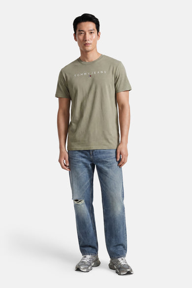 Groene korte mouw T-shirt van TOMMY JEANS met wit logo op borst, gedragen met gescheurde jeans en grijze sneakers, front view