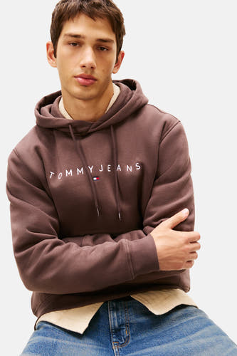 Gilet brun avec capuche de TOMMY JEANS, avec logo blanc de la marque sur la poitrine et jeans bleus visibles.