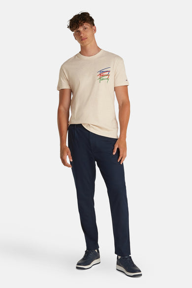 Beige T-shirt met korte mouwen van TOMMY JEANS, met een gekleurd logo en gecombineerd met een donkerblauwe broek en schoenen.