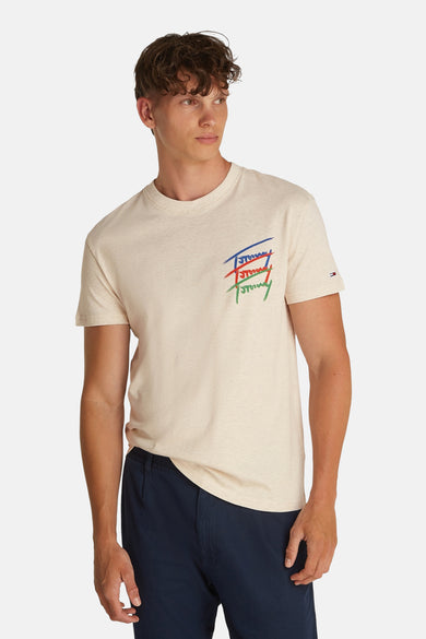 Beige T-shirt met korte mouwen van TOMMY JEANS, met kleurrijk logo op de borst en gedragen met een donkerblauwe broek.