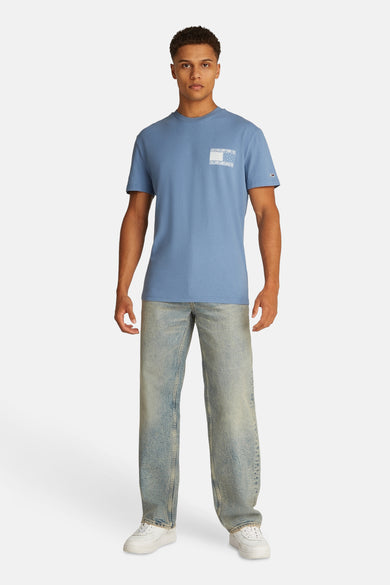 T-shirt bleu à manches courtes de TOMMY JEANS, avec un poche décorative et associé à un jean et des baskets blanches.