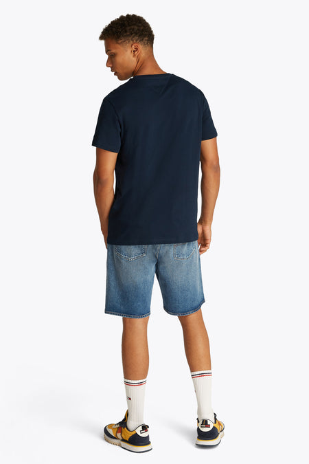 T-shirt bleu à manches courtes de TOMMY JEANS, dos, associé à des shorts en denim, des chaussettes blanches et des baskets colorées.
