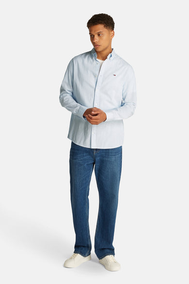 Lichtblauw overhemd met lange mouwen van Tommy Jeans, met donkerblauwe jeans en witte sneakers.