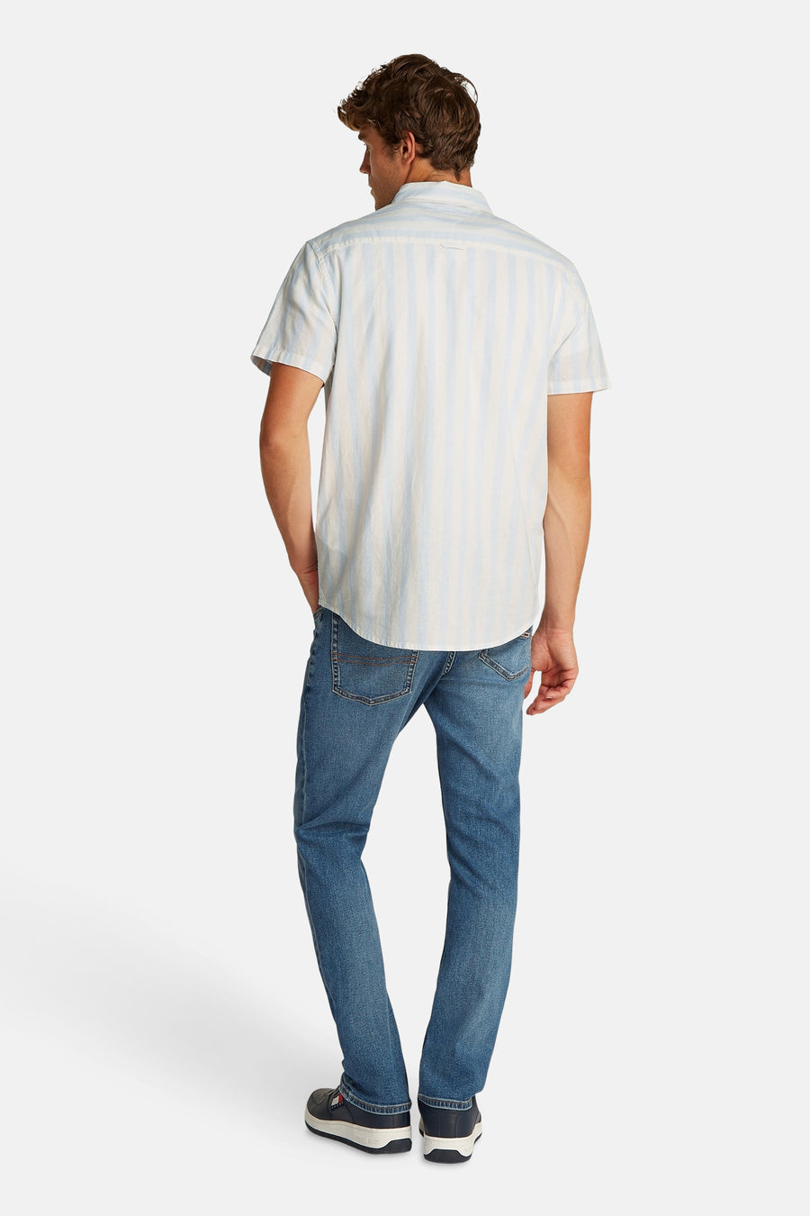 Blauw gestreept overhemd met korte mouwen van TOMMY JEANS, gedragen met blauwe jeans en donkerblauwe sneakers, gezien van achteren.