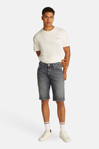 Shorts en denim noir de TOMMY JEANS, portés avec un T-shirt blanc, des chaussettes blanches à rayures et des sneakers blanches.