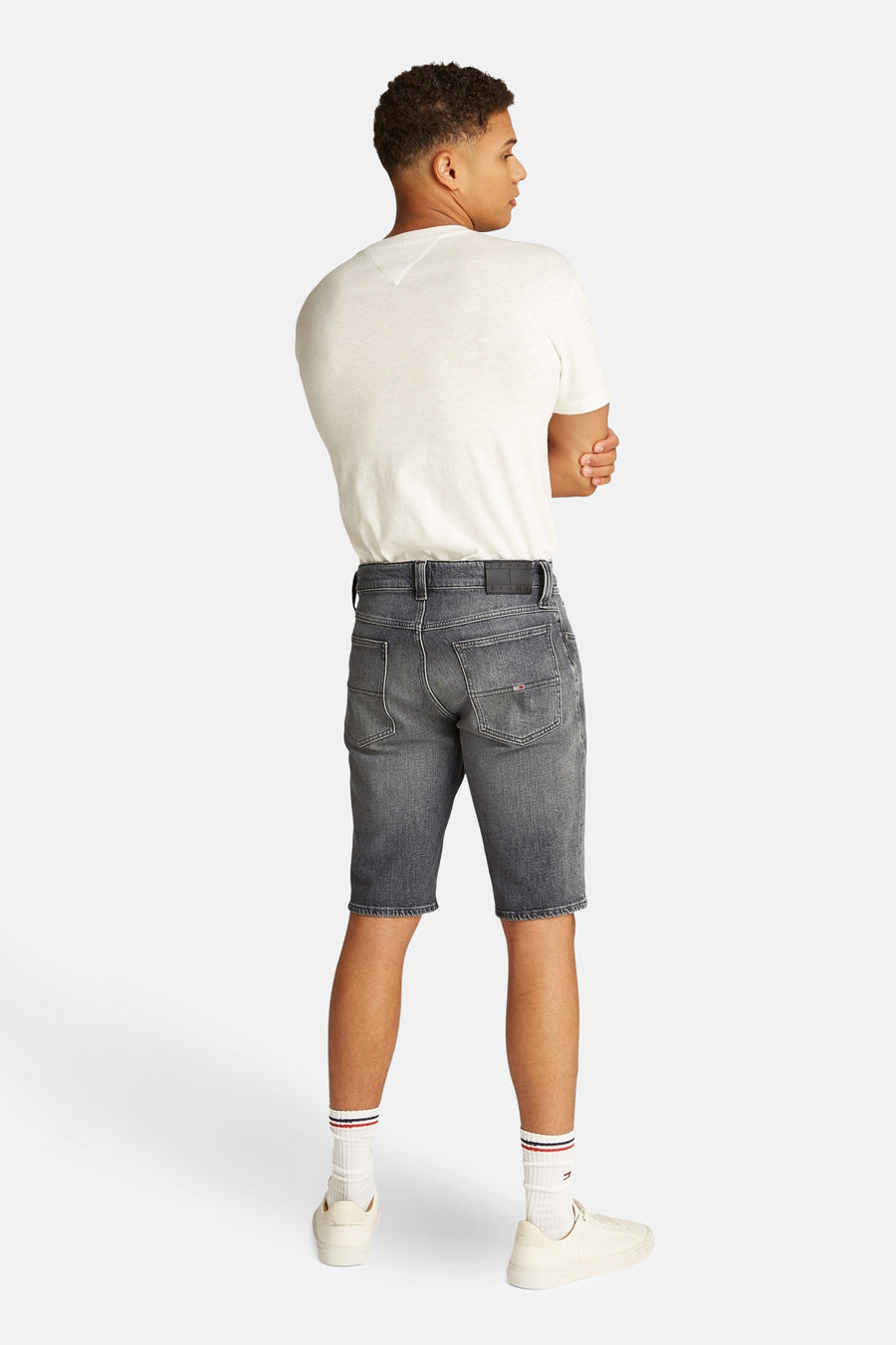 Jean denim noir court de Tommy Jeans, avec des détails sur l'arrière, porté avec un T-shirt blanc et des baskets coordonnées.