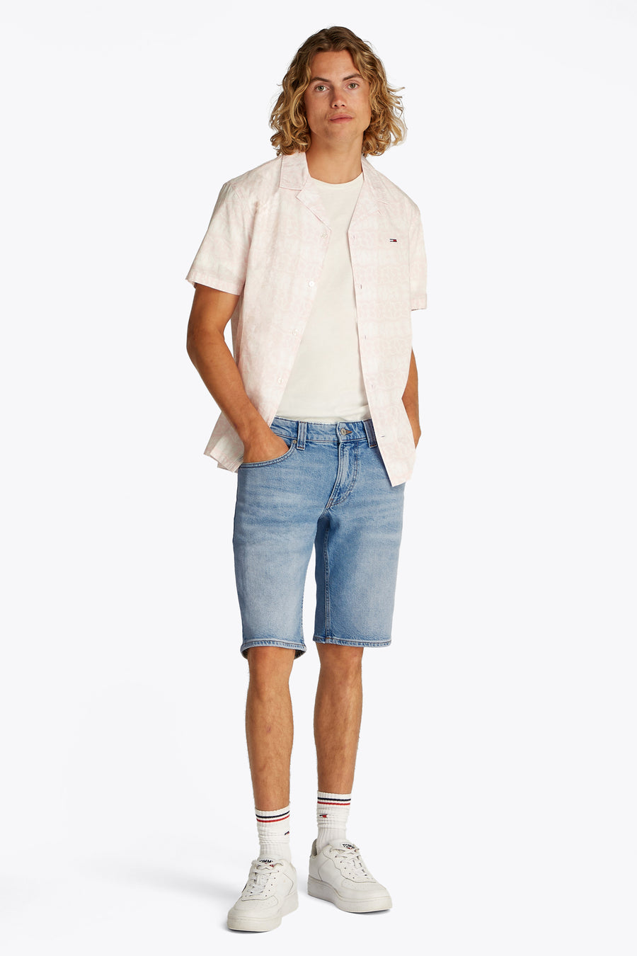 Jeansshort van lichtblauwe denim van TOMMY JEANS, met korte pijpen en gedragen met een wit T-shirt en een roze overhemd.
