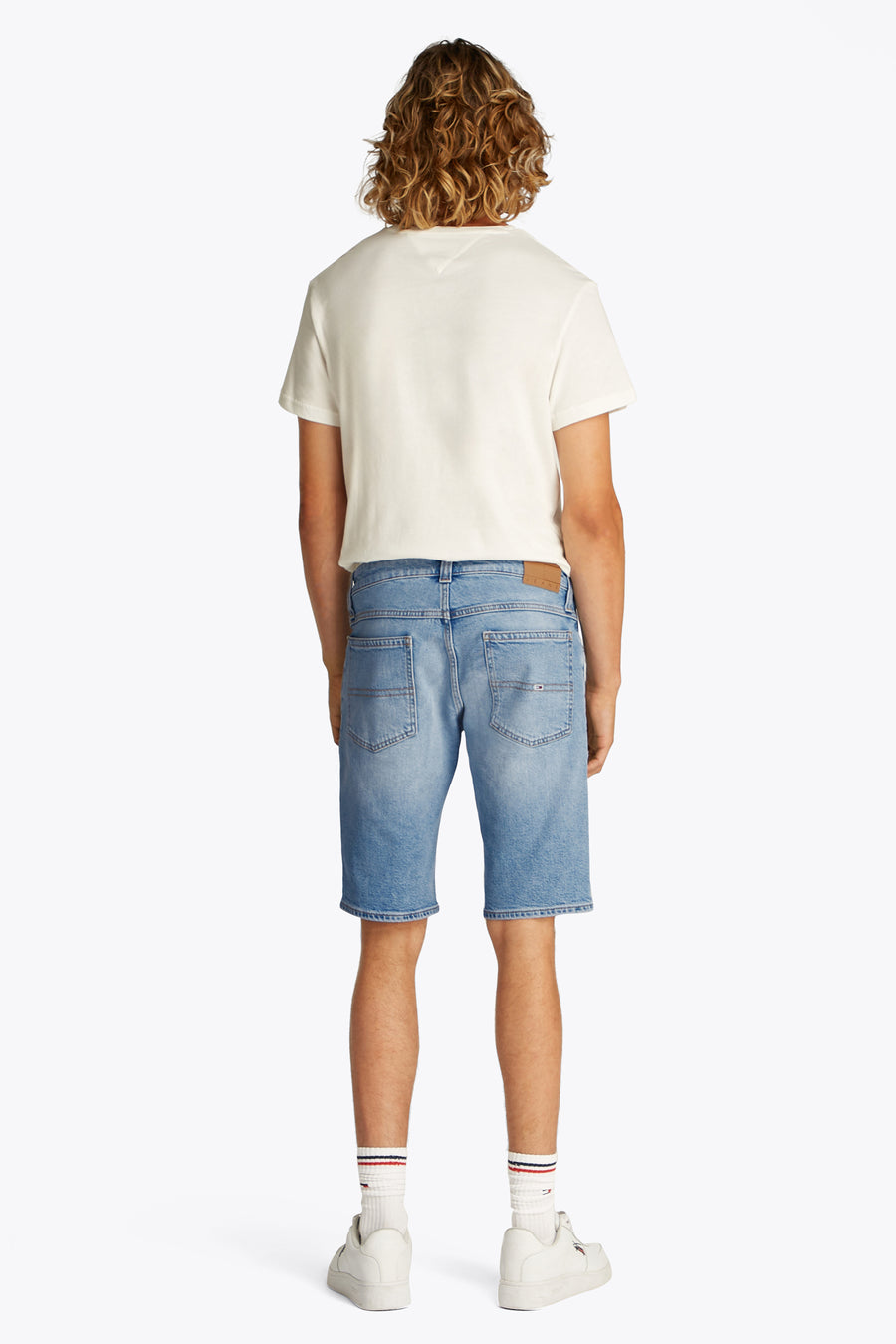 Jeansshort van lichtblauw denim van TOMMY JEANS, gezien van achteren, met witte sneakers en sokken met strepen.
