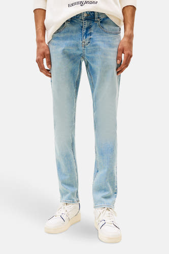 Jean slim de denim bleu clair de TOMMY JEANS, avec des baskets blanches et un pull.