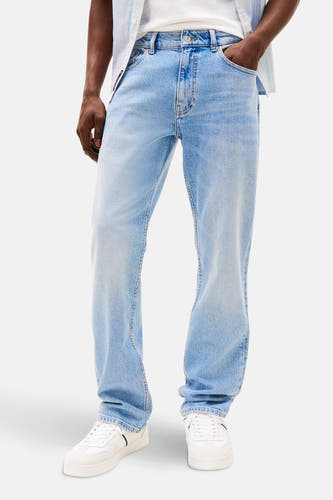 Rechte jeans van lichtblauw denim van TOMMY JEANS, met witte sneakers en een gestreept overhemd.
