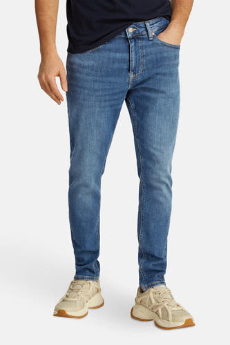 Jean tapered bleu clair de TOMMY JEANS, avec un léger lavage et porté avec des baskets blanches.