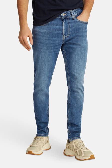 Jean tapered bleu clair de TOMMY JEANS, avec un léger lavage et porté avec des baskets blanches.