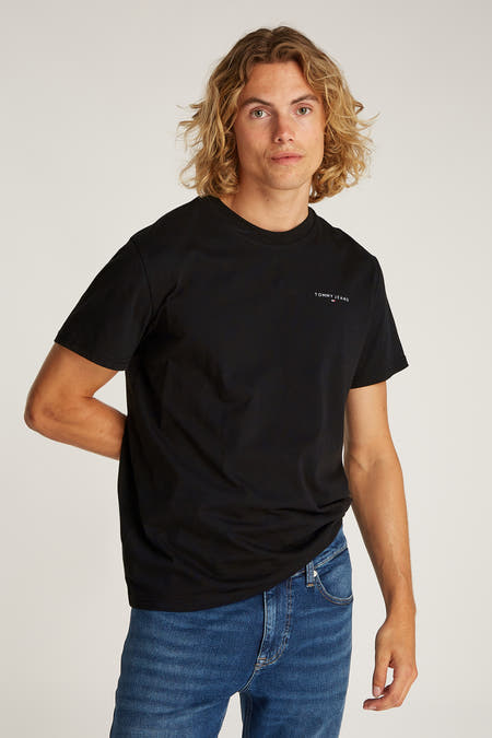 Zwart T-shirt met korte mouwen van TOMMY JEANS, gedragen met een blauwe jeansbroek.

