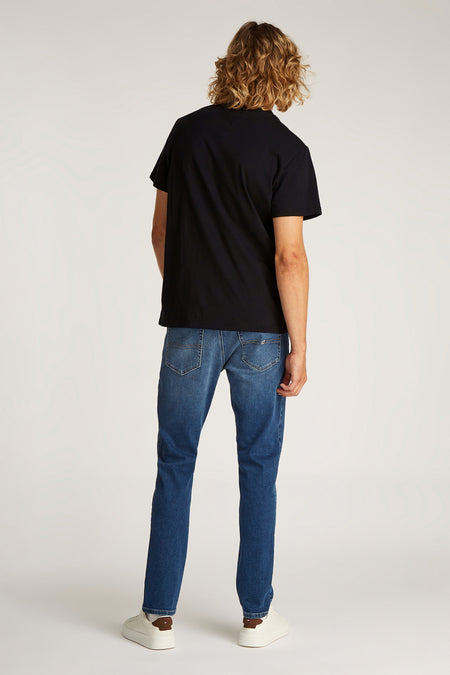 Zwart T-shirt met korte mouwen van TOMMY JEANS, gezien van achteren met blauwe jeans en witte sneakers.