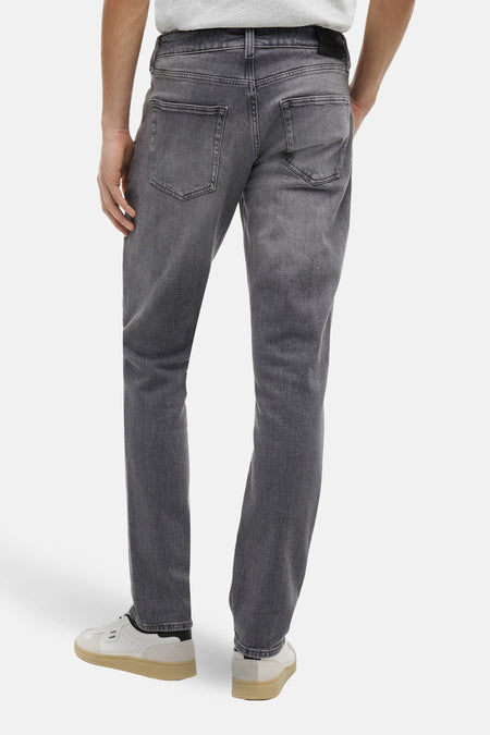 Slim jeans in donkergrijs denim van TOMMY JEANS, achterkant gezien, met subtiele wassing en casual schoenen.