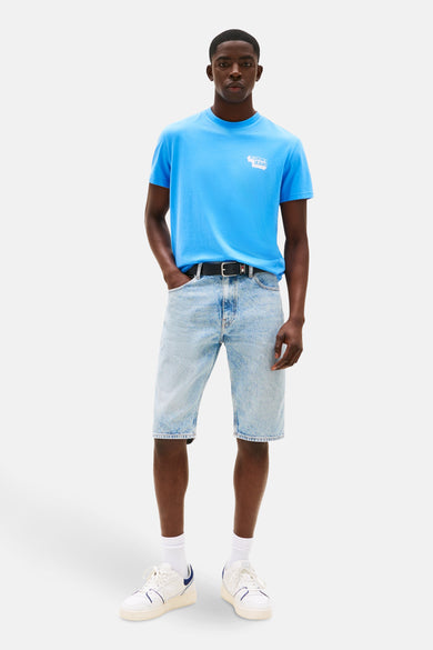 T-shirt bleu à manches courtes de TOMMY JEANS, porté avec des shorts en denim, des chaussettes blanches et des baskets.