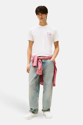 T-shirt écru à manches courtes de TOMMY JEANS, avec logo rose, associé à des jeans larges et un gilet rose autour de la taille.
