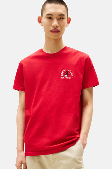 T-shirt rouge à manches courtes de TOMMY JEANS, avec une petite impression "New York City" sur la poitrine, porté avec un pantalon beige.