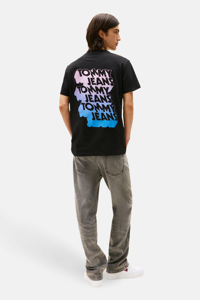 Zwart T-shirt met korte mouwen van TOMMY JEANS, met kleurrijke logo-opdruk op de rug, gecombineerd met grijze jeans en witte sneakers.