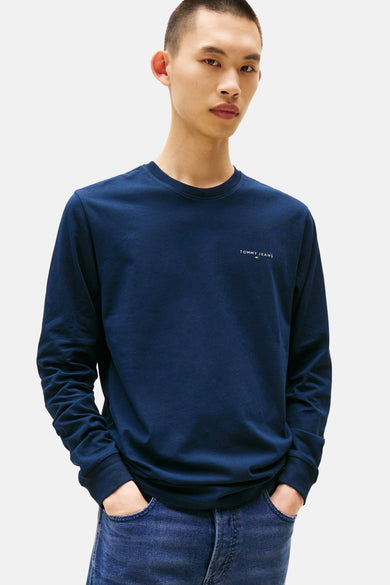 T-shirt bleu à manches longues de TOMMY JEANS, avec un logo subtil sur la poitrine et porté avec des jeans.