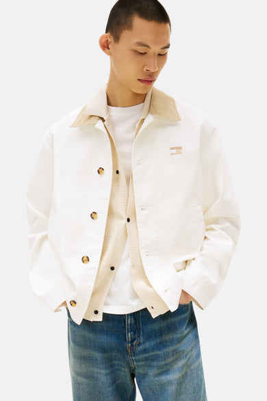 Mauve court manteau de TOMMY JEANS, avec un col en corduroy beige et porté sur une chemise crème et des jeans bleus.