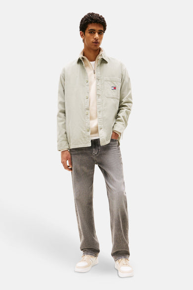 Groen overhemd met lange mouwen van Tommy Jeans, met een subtiele corduroy textuur. De man draagt een witte sweater en grijze jeans.