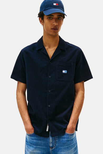 Chemise en corduroy bleu TOMMYMY JEANS avec man mantestestes poche poitrine, portée avec un chapeau bleu et des jeans.
