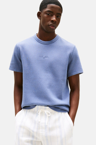 T-shirt bleu à manches courtes de TOMMY JEANS, avec une subtile texture et porté avec un short rayé.