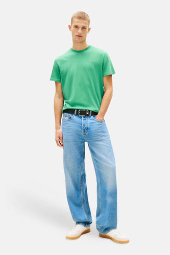 Groen T-shirt met korte mouwen van TOMMY JEANS, met een ronde hals en gedragen met wijde jeans en witte sneakers.
