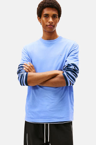 T-shirt bleu de TOMMY JEANS, avec des manches courtes et associé à un t-shirt rayé à longs manches.