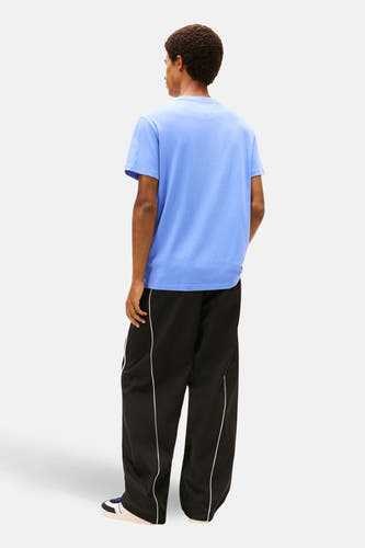 T-shirt bleu (manches courtes) de TOMMY JEANS, porté avec un short d'entraînement noir à rayures blanches.