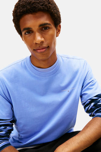 T-shirt bleu à manches courtes de Tommy Jeans, porté avec un chemisier rayé en dessous.
